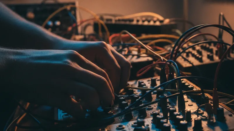 Hands adjusting knobs on a modular synthesizer in a dim home studio with patch cables
